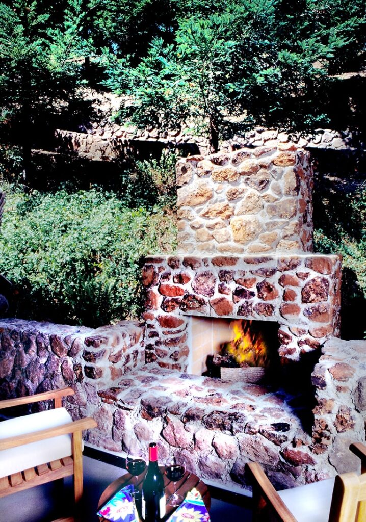 Cozy outdoor stone fireplace surrounded by greenery